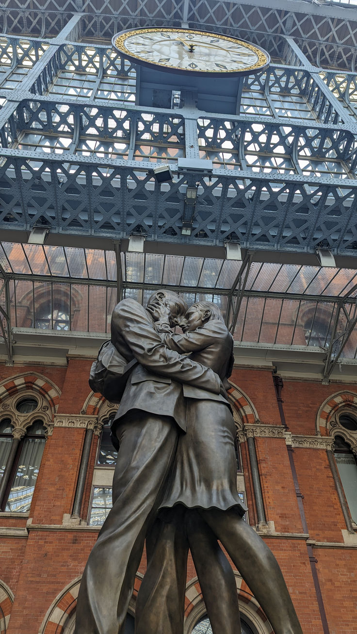 a statue of a man holding a woman in front of a building with a clock