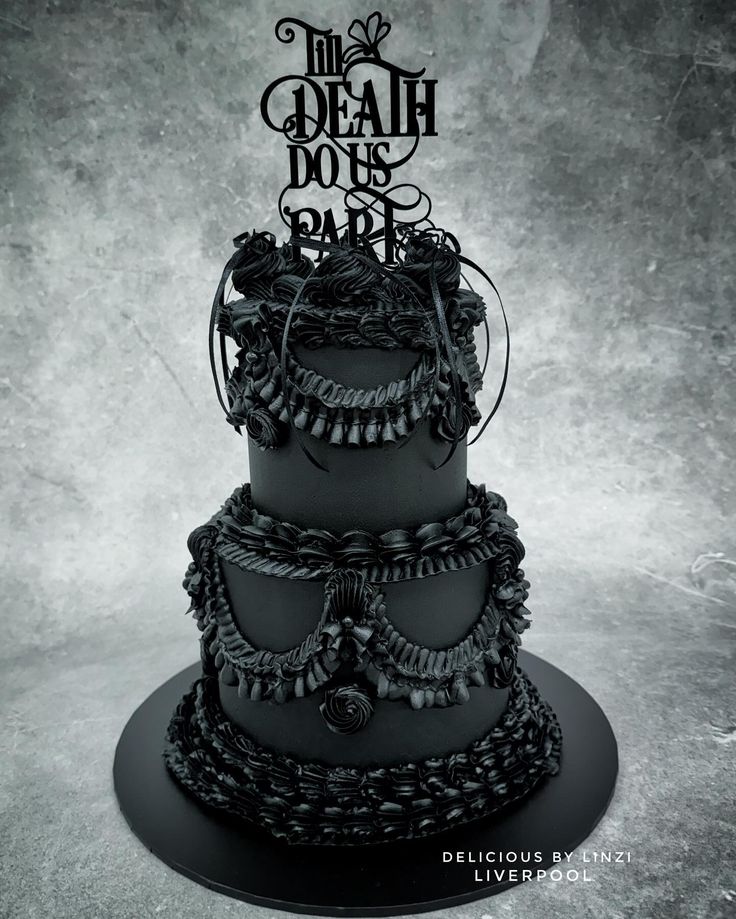 a three tiered cake decorated with black icing and metal decorations is shown in front of a gray background