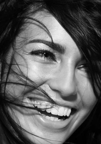 a woman smiling with her hair blowing in the wind while she is wearing a black and white photo