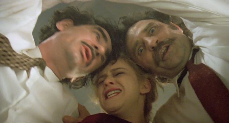 three men and a woman laying in bed with their heads on each other's shoulders