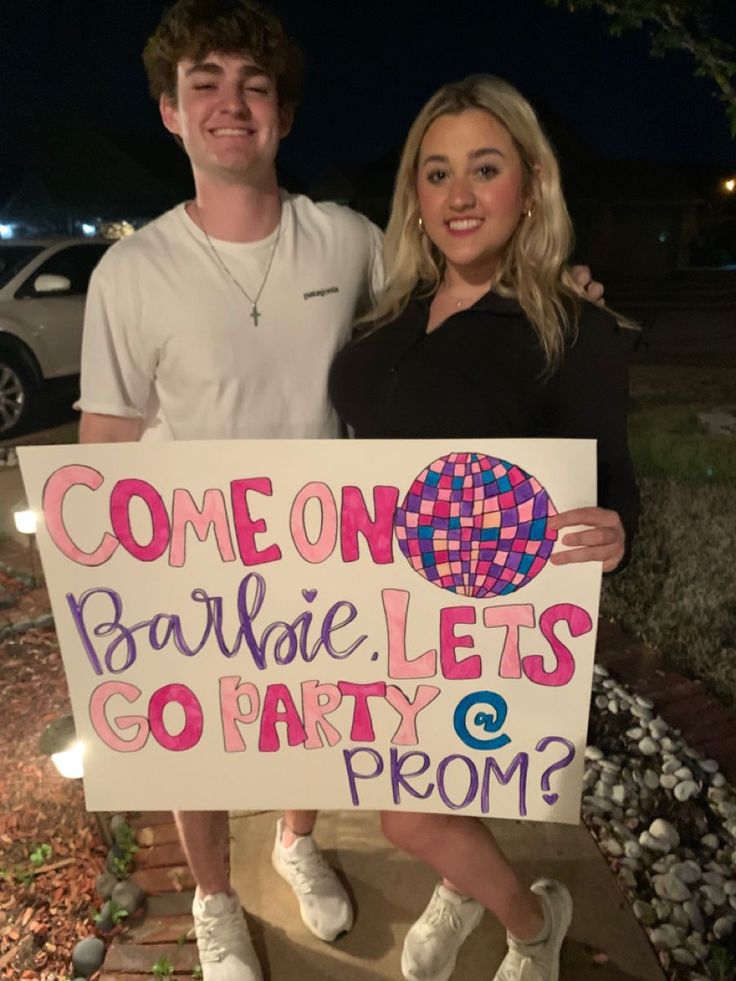 two people standing next to each other holding a sign that says someone parties go party & prom?