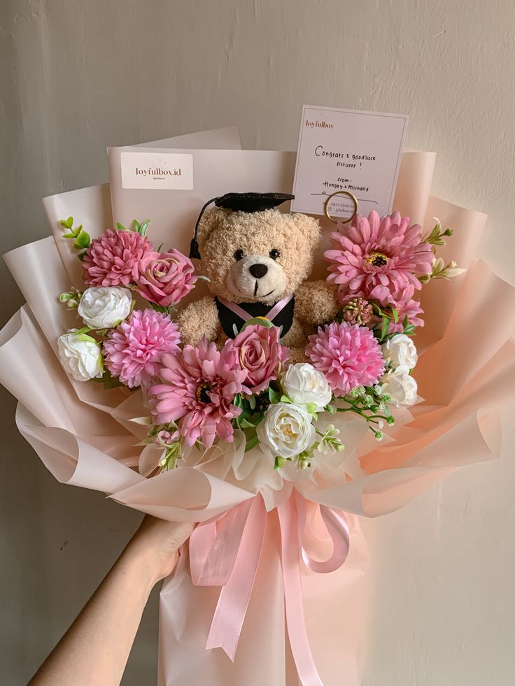 a teddy bear sitting on top of a bouquet of pink and white flowers next to a card