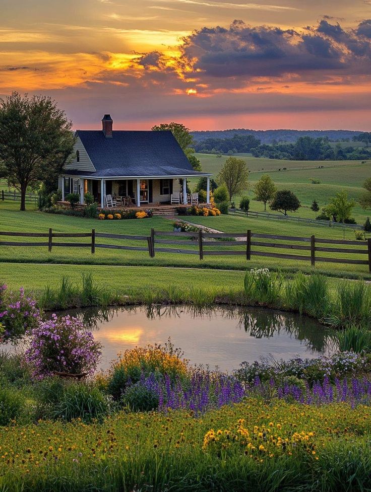 a farm house with a pond in the foreground and flowers on the other side