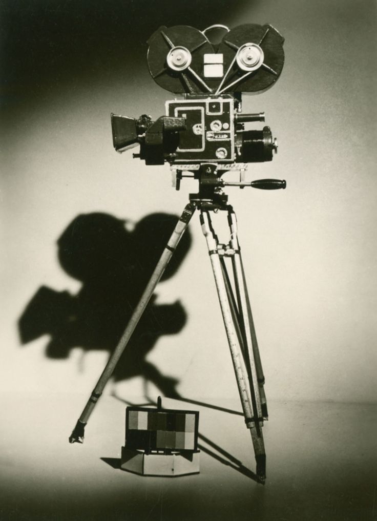 an old fashioned movie camera on a tripod with a shadow from the film behind it