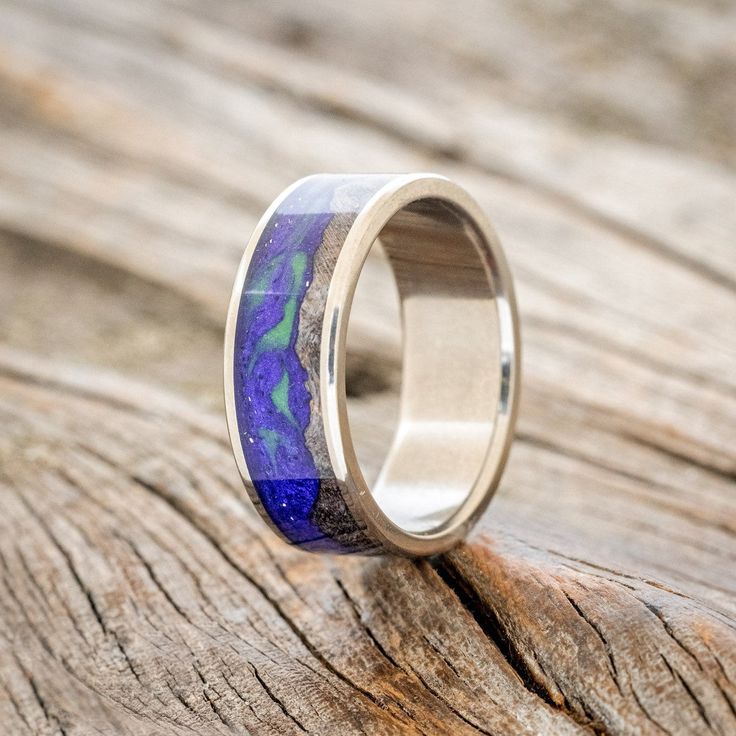 a wedding ring with blue and purple marble inlays on it sitting on a piece of wood