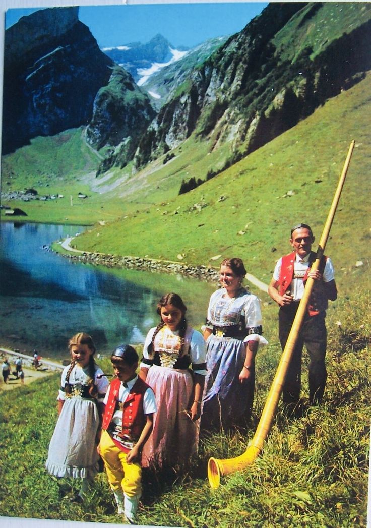 a group of people standing on top of a grass covered hillside next to a lake