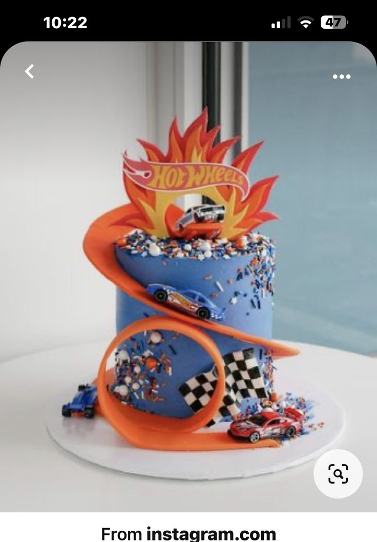 a birthday cake with cars on top and hot wheels decoration around the edges, sitting on a white table