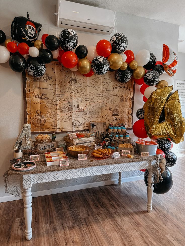 a table topped with lots of desserts and balloons in the shape of pirate's chest