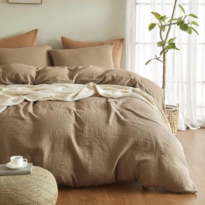 a bed with brown linens and pillows in a white room next to a potted plant