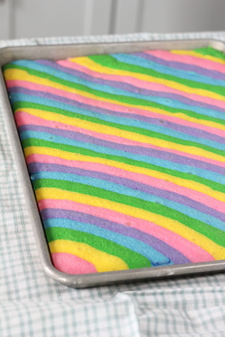 a pan filled with rainbow colored cake on top of a checkered table cloth