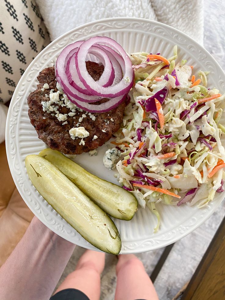 a white plate topped with meat, coleslaw and cucumber next to a pickle