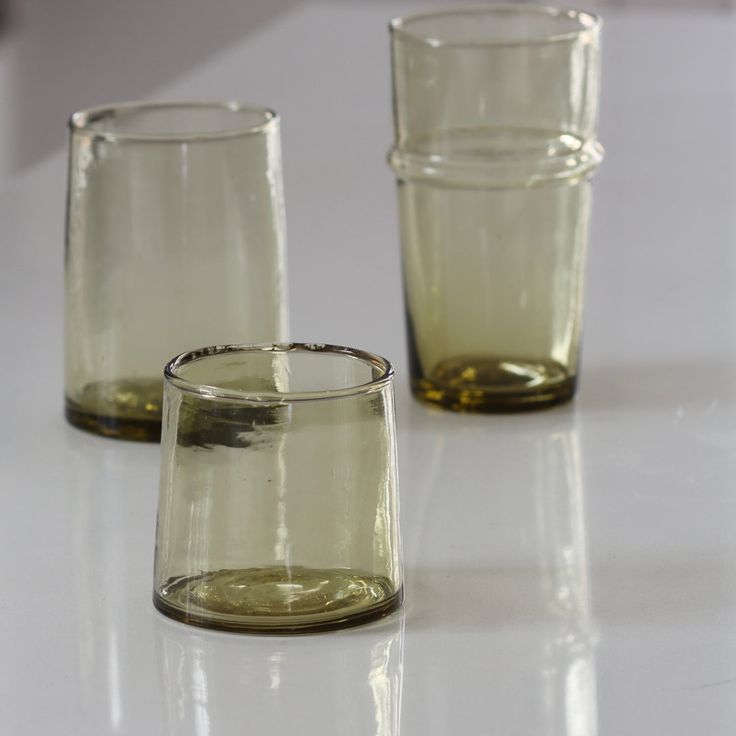 three glasses sitting on top of a white table next to each other and one is empty