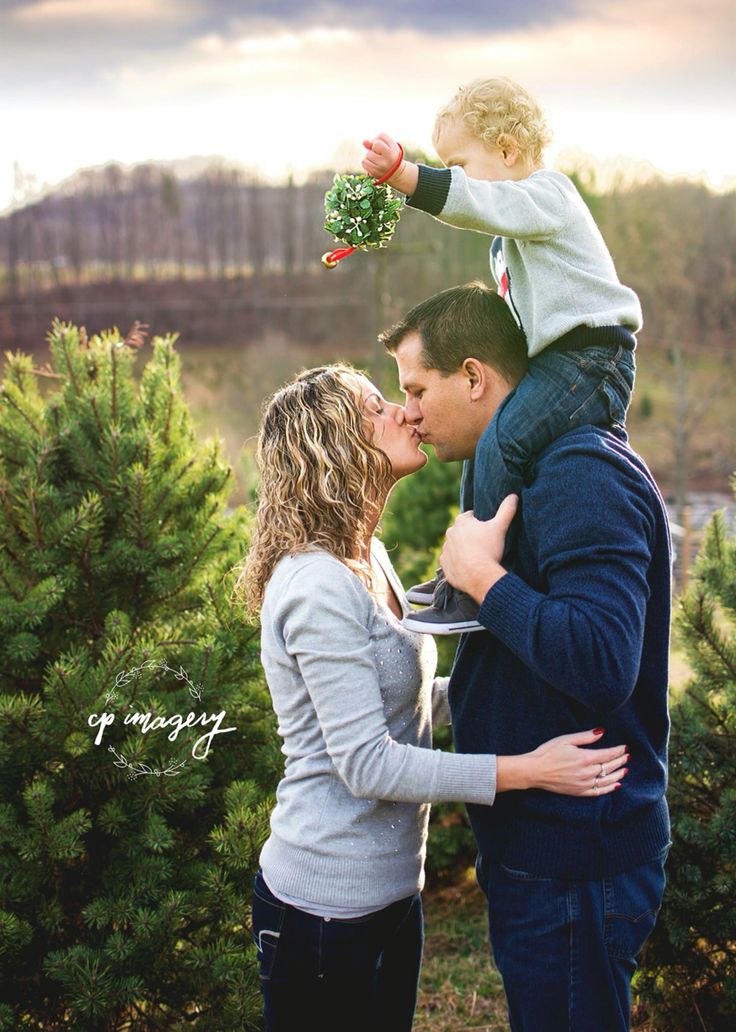 a man and woman kissing their son in front of christmas trees