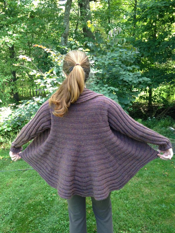 a woman is standing in the grass with her back to the camera, wearing a purple sweater