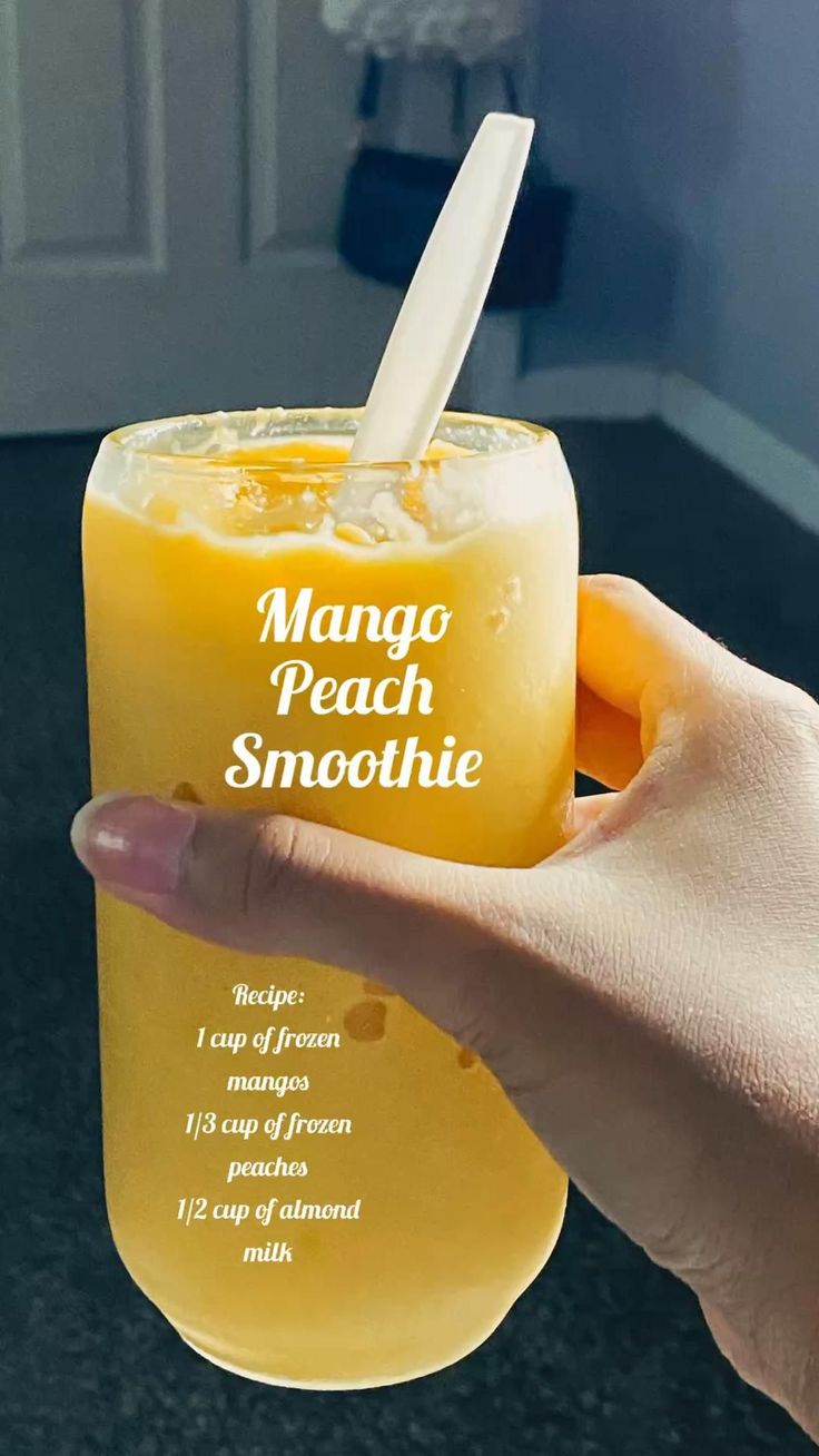 a person holding up a glass with mango peach smoothie in it's hand