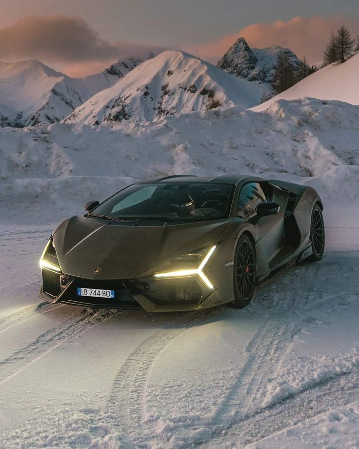 a very nice looking sports car driving through the snow covered ground with mountains in the background