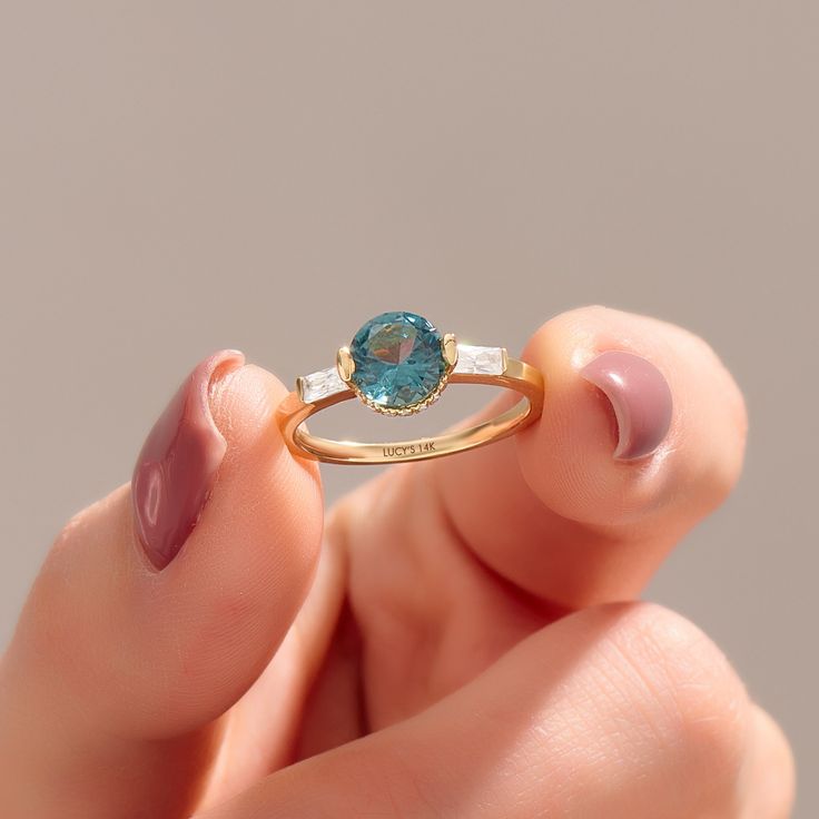 a woman's hand holding a ring with a blue stone