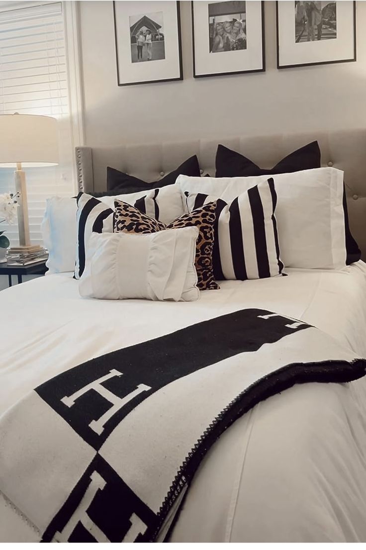 a bed with black and white pillows on top of it next to two framed pictures