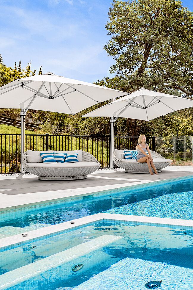 a woman sitting under an umbrella next to a swimming pool with chaise lounges