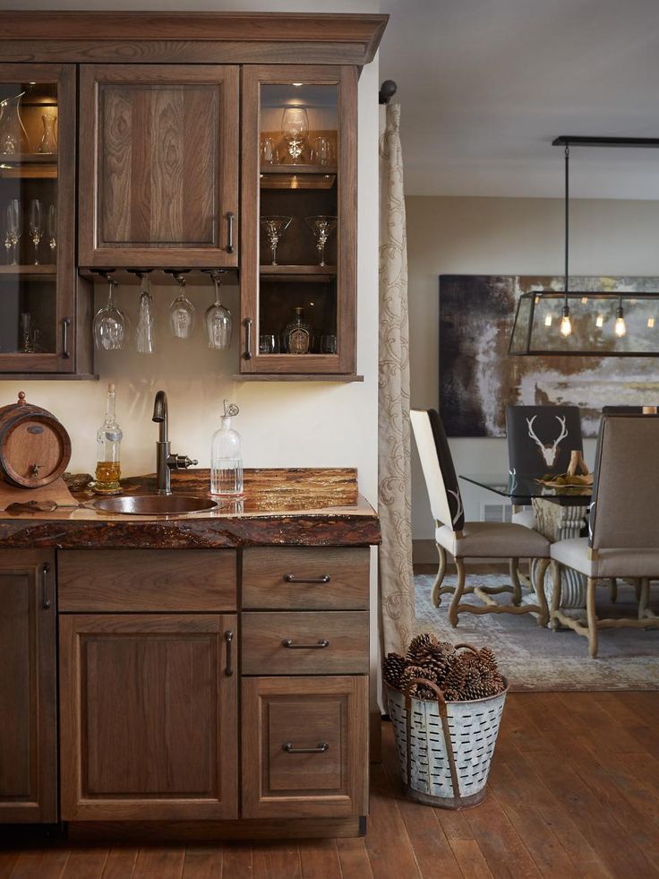 a kitchen with wooden cabinets and glassware on the counter top, in front of a dining room table