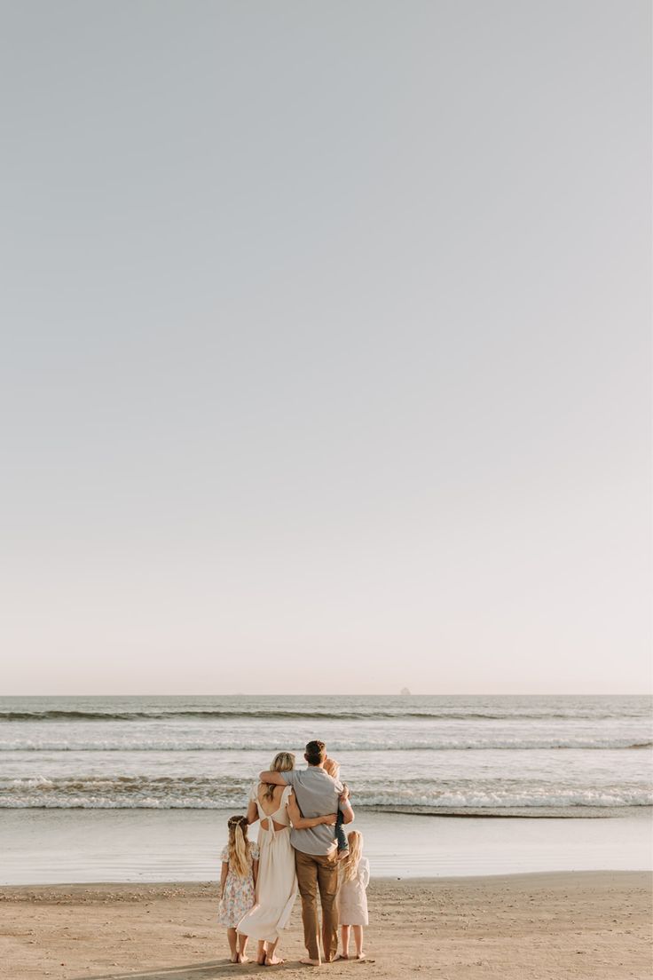 a family standing on the beach with their arms around each other and looking at the ocean