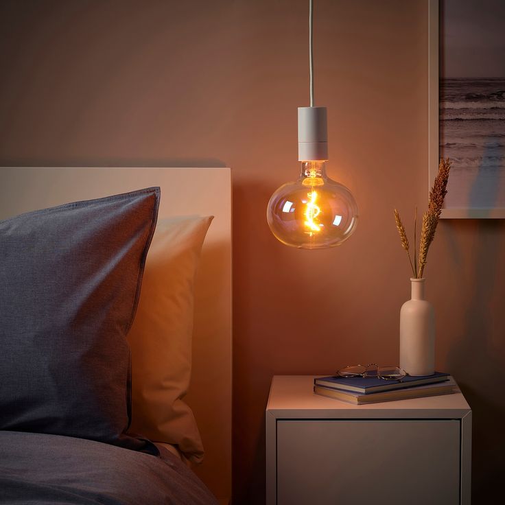 a light bulb hanging over a bed next to a night stand with a plant in it