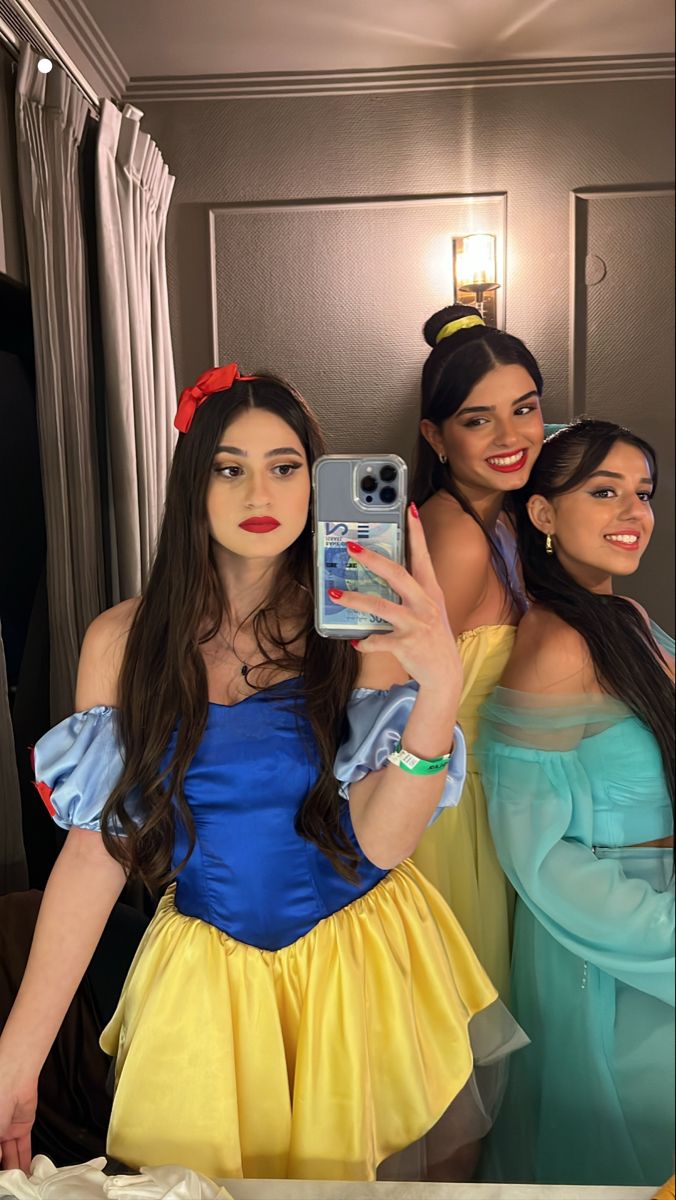 three women dressed up in costumes taking a selfie with a cell phone while standing next to each other