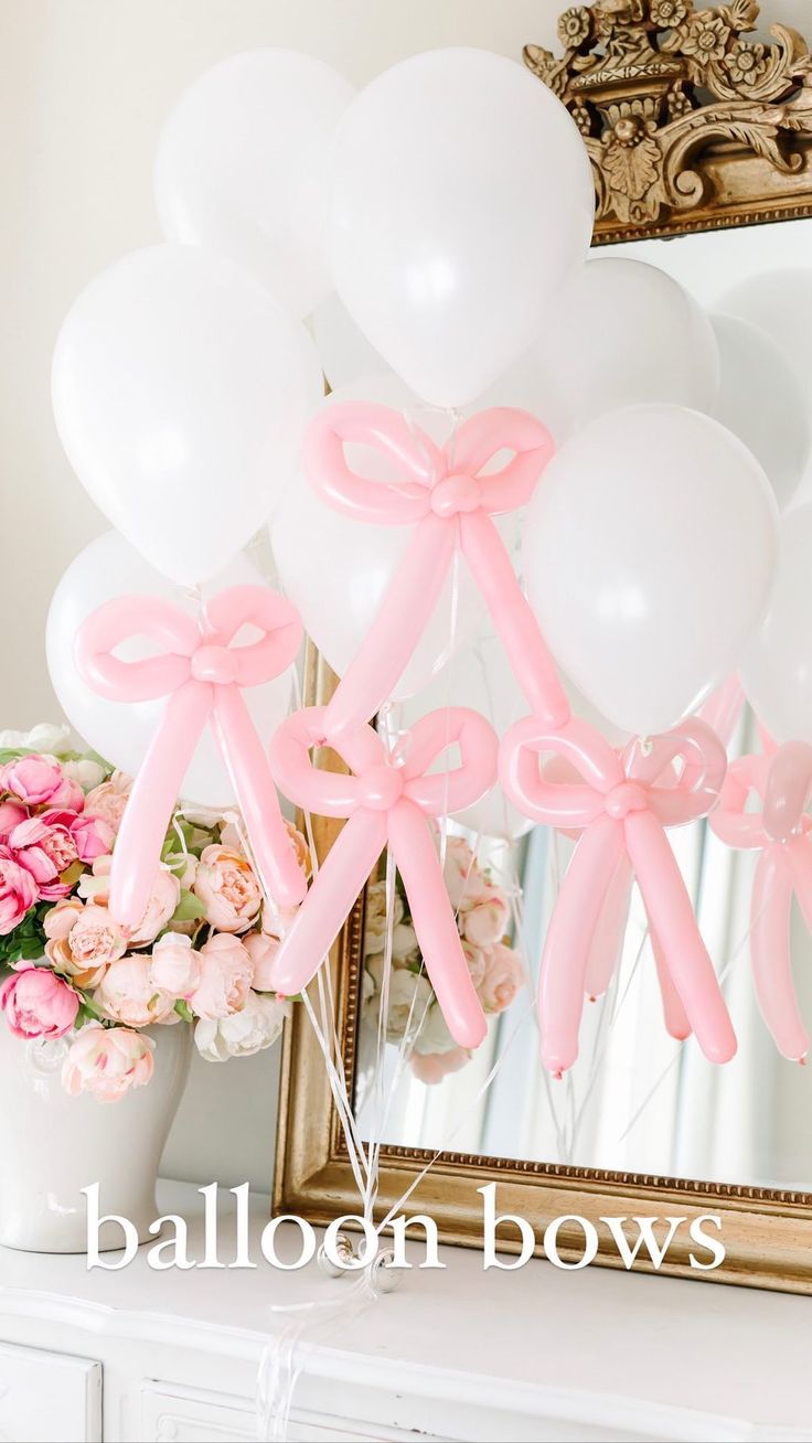 balloons tied to the side of a mirror with pink bows on them and flowers in vase