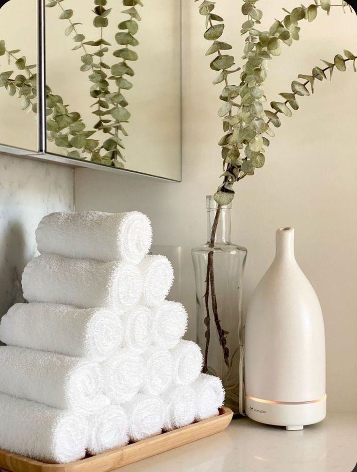 white towels are stacked on a tray next to a vase with flowers and a mirror in the background