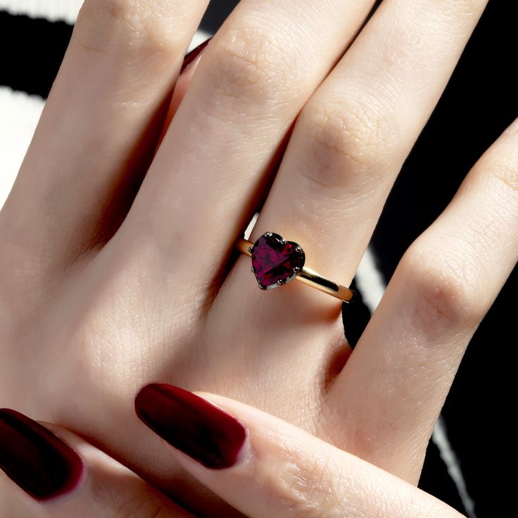 a woman's hand with red nail polish holding a heart shaped ring on her finger