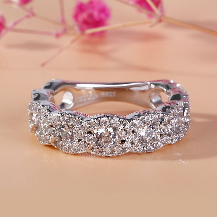 a wedding band with three rows of diamonds on it and pink flowers in the background