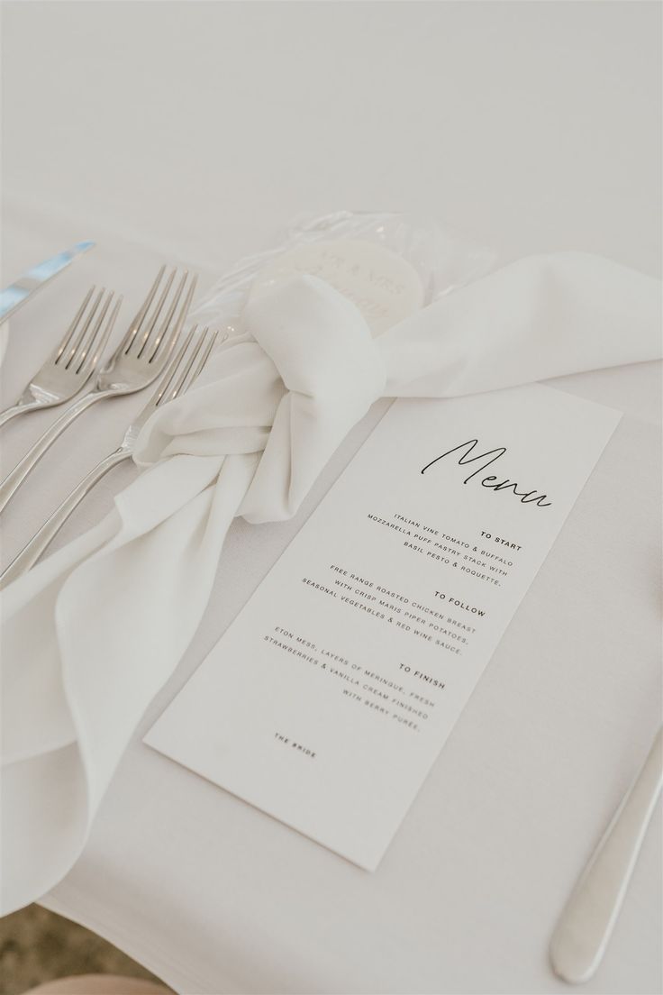 a table set with silverware and napkins on top of white cloth covered place settings