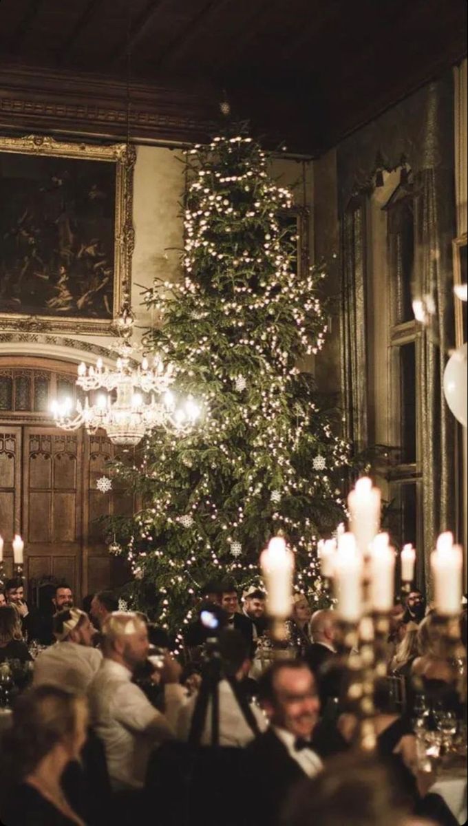 a group of people sitting around a table in front of a christmas tree with lights on it