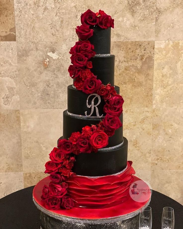 a three tiered black and red wedding cake with roses on top, sitting on a table