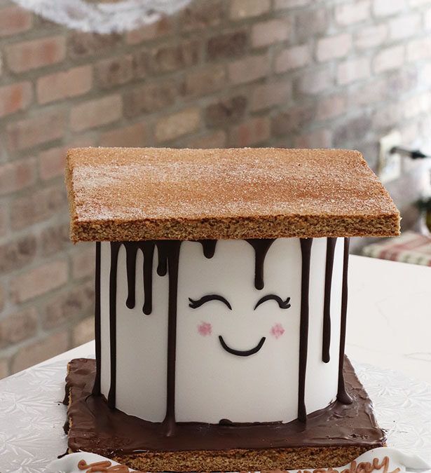 a cake with chocolate drips on it sitting on top of a white table next to a brick wall