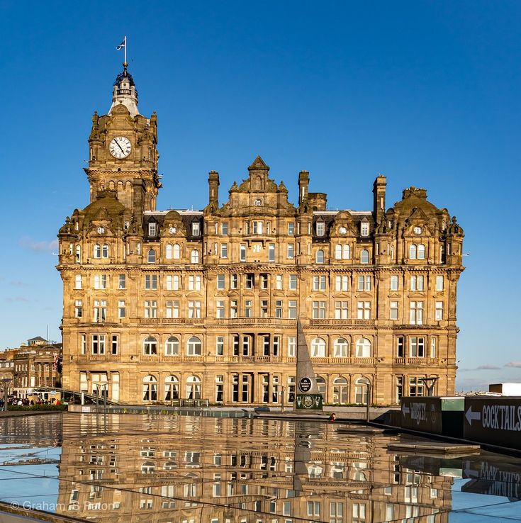 a large building with a clock on the top of it's tower and reflecting in water