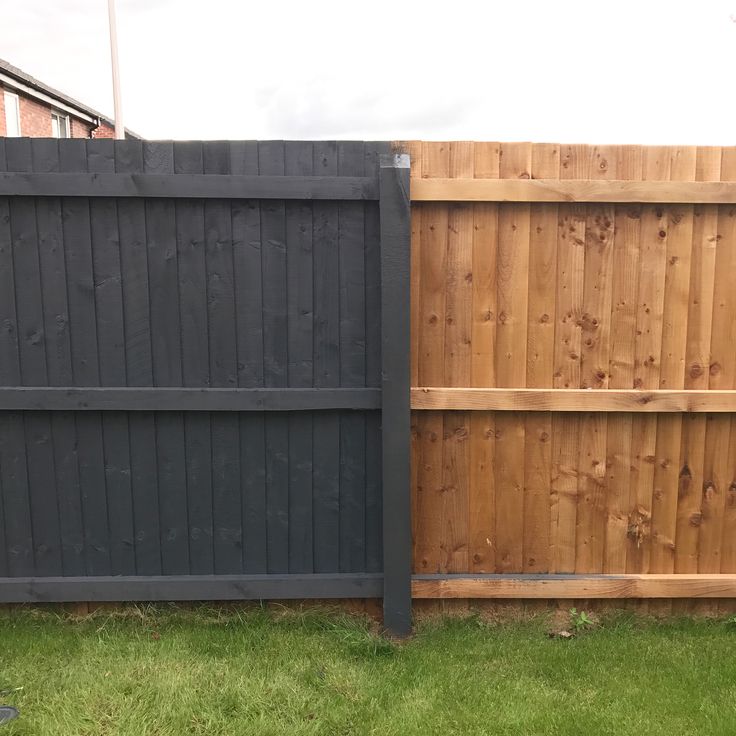 a wooden fence in the grass next to a tall black fence with vertical slats