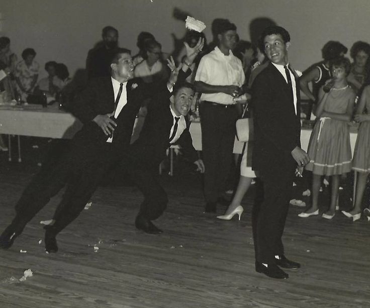 two men in suits and ties dancing on a wooden floor with people standing around them