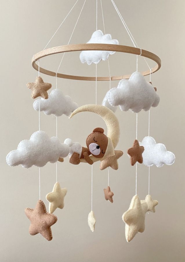 a teddy bear is sitting on the moon and stars mobile hanging from a wooden rod