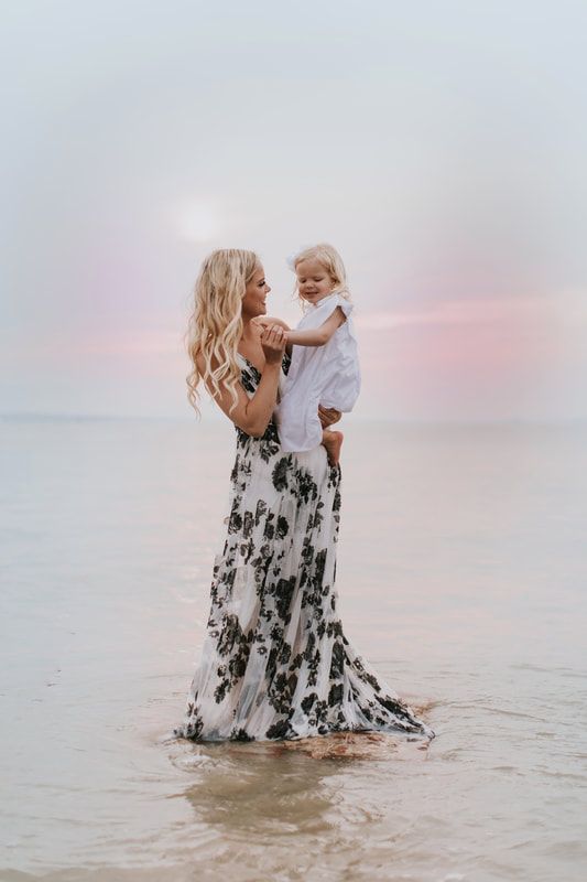 a woman holding a baby in her arms while standing in the ocean