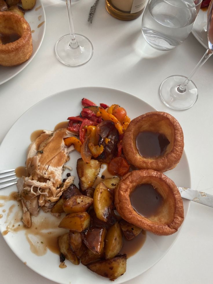 a white plate topped with meat and potatoes covered in gravy next to wine glasses