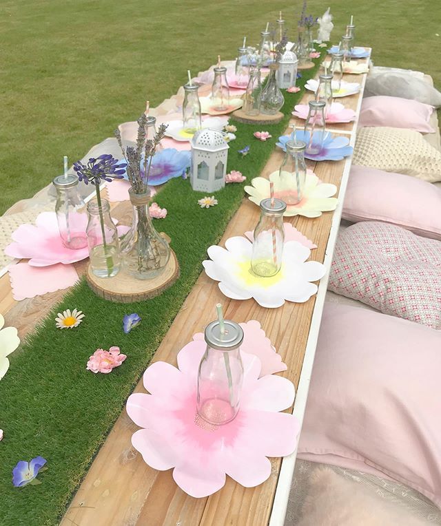 a long table set up with pink and white flowers on the grass for an outdoor party