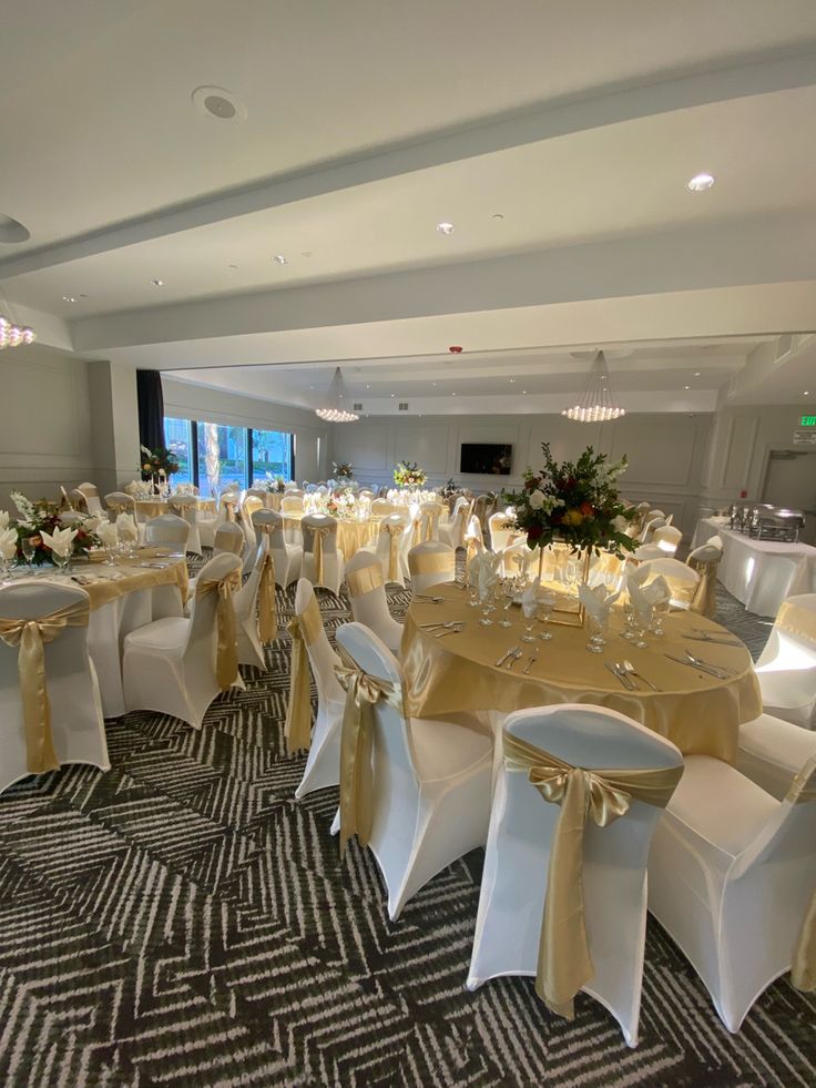 the banquet room is set up with white and gold tablecloths, chairs, and centerpieces