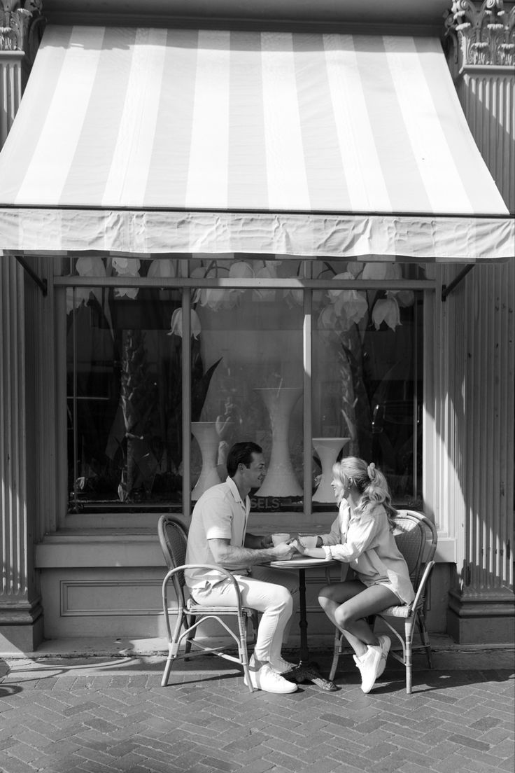 black and white photograph of two people sitting at a table in front of a store