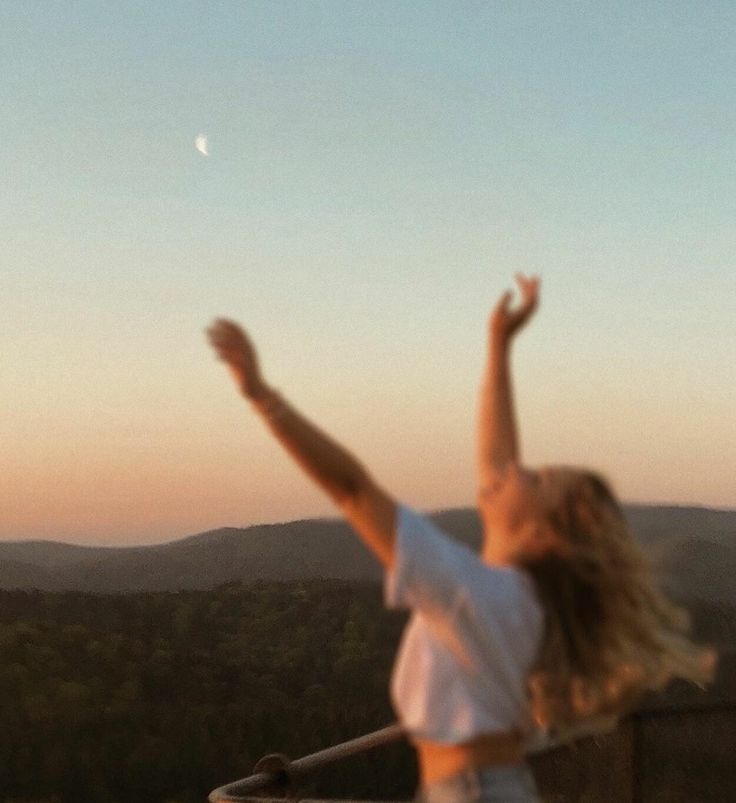 a woman standing on top of a balcony holding her arms in the air