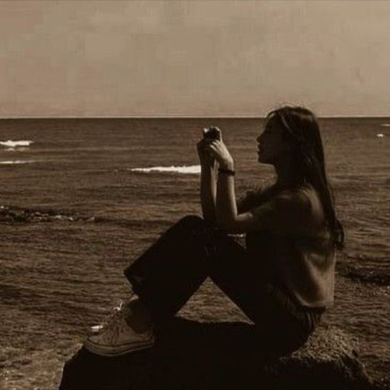 a woman sitting on top of a rock next to the ocean