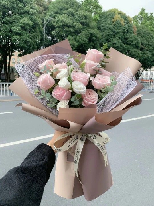 a bouquet of pink and white roses is being held up by someone's hand