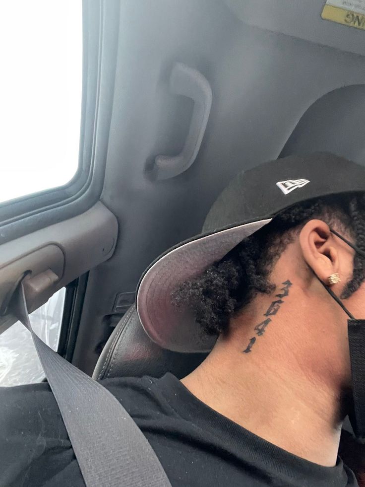 a man with a hat and tattoos on his head sitting in the back seat of a car