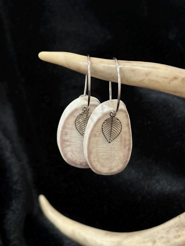 two wooden earrings with leaves on them hanging from a twig, against a black background