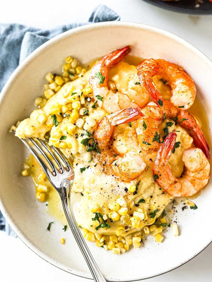 a white bowl filled with shrimp, corn and grits on top of a table